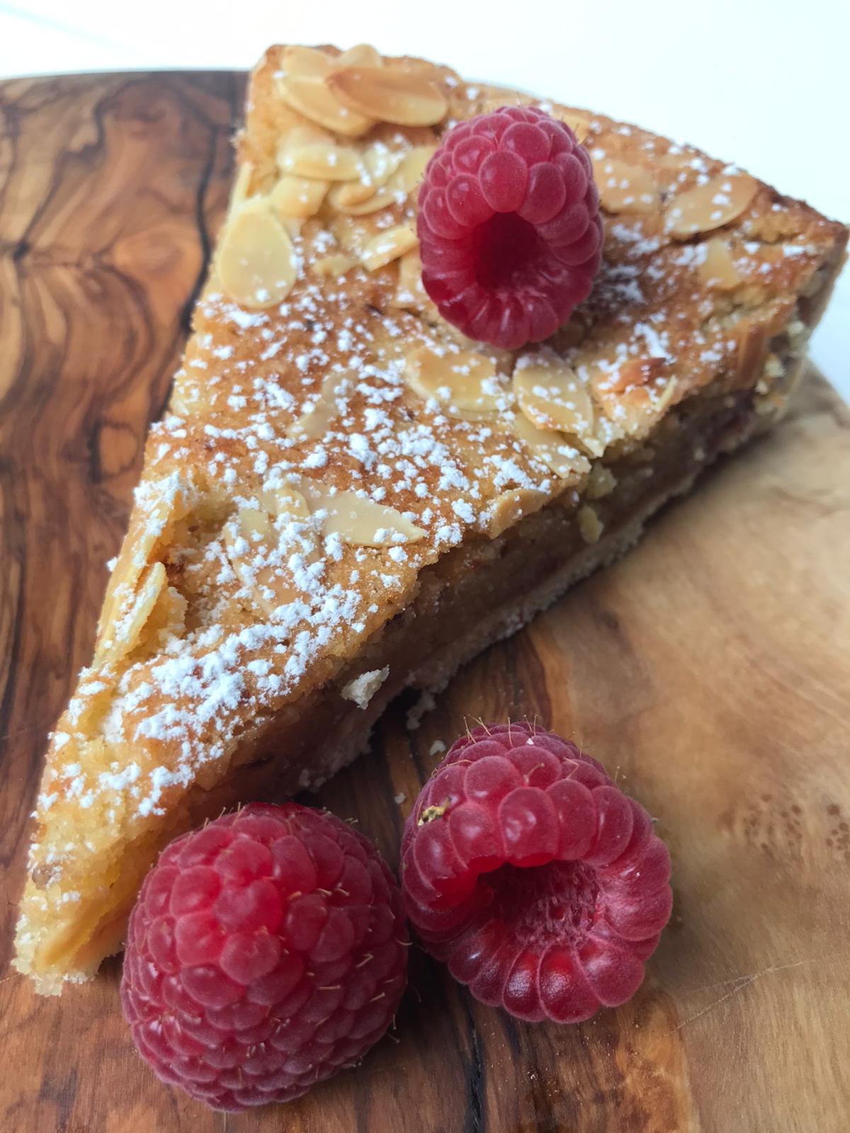 A tempting slice of vegan Bakewell Tart, showcasing its flaky pastry, vibrant raspberry jam, and creamy almond filling.
