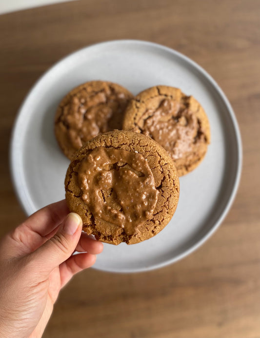 A plate of three round, golden-brown vegan salted Biscoff cookie with visible specks of Biscoff crumbs and a sprinkle of sea salt on top.