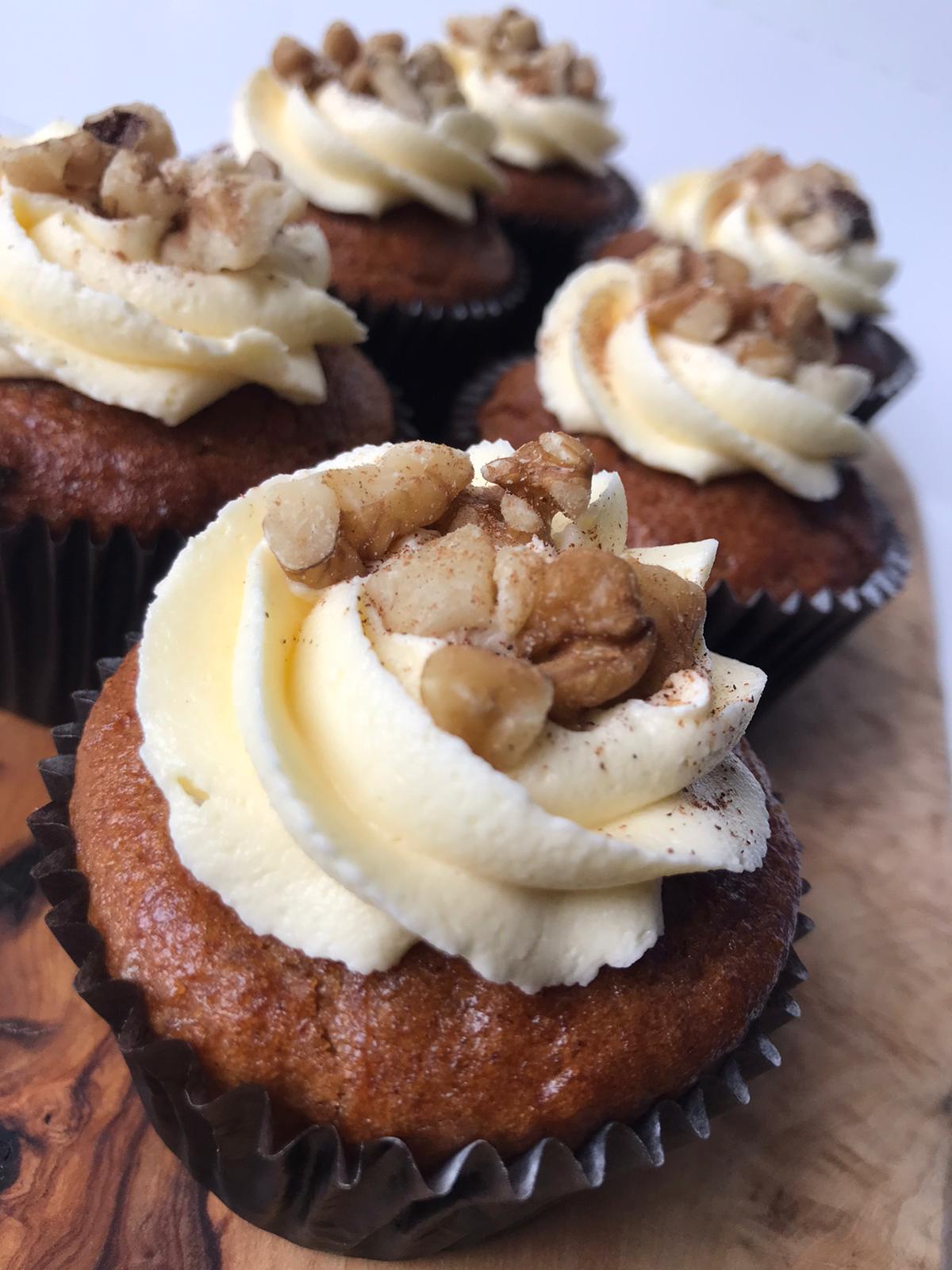 Vegan carrot cupcakes, topped with swirls of creamy frosting and sprinkled with chopped walnuts.