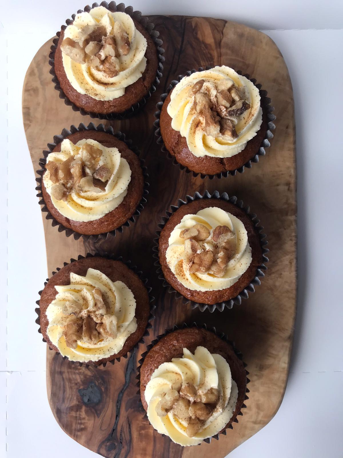 Six delectable vegan carrot cupcakes, topped with swirls of creamy frosting and sprinkled with chopped walnuts.