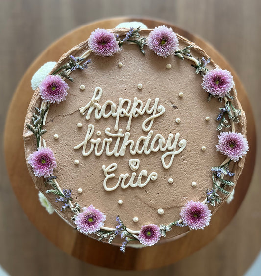 Chocolate custom vegan cake reading happy birthday Eric with flowers around.