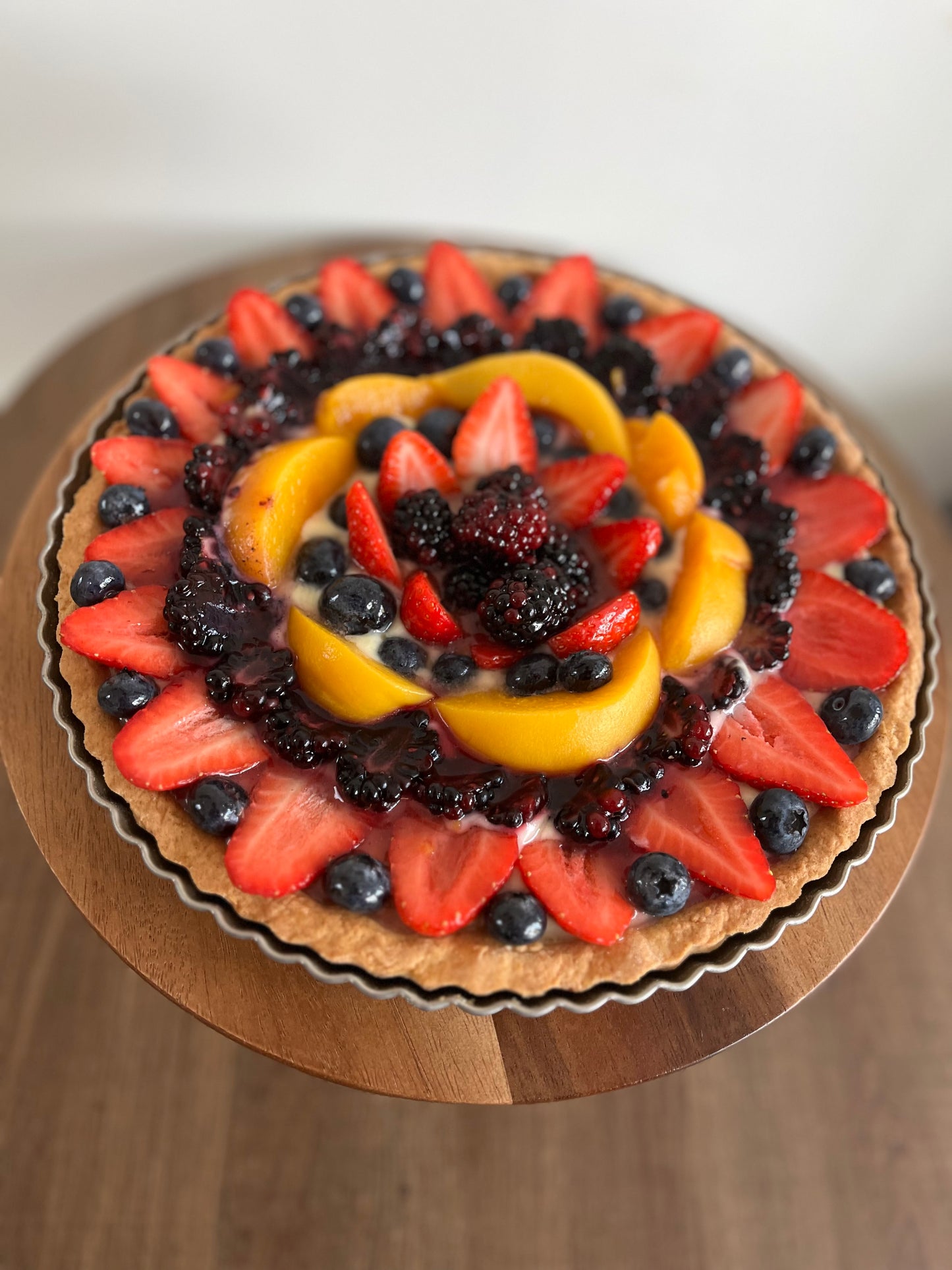 A vibrant vegan fresh fruit tart, featuring a colorful assortment of berries and other seasonal fruits arranged on a golden-brown pastry crust.