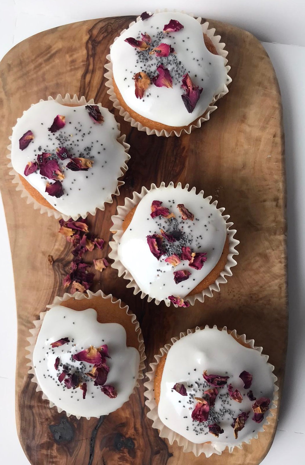 Five vegan Lemon & Poppy Seed Cupcakes, each with a light yellow top sprinkled with poppy seeds.