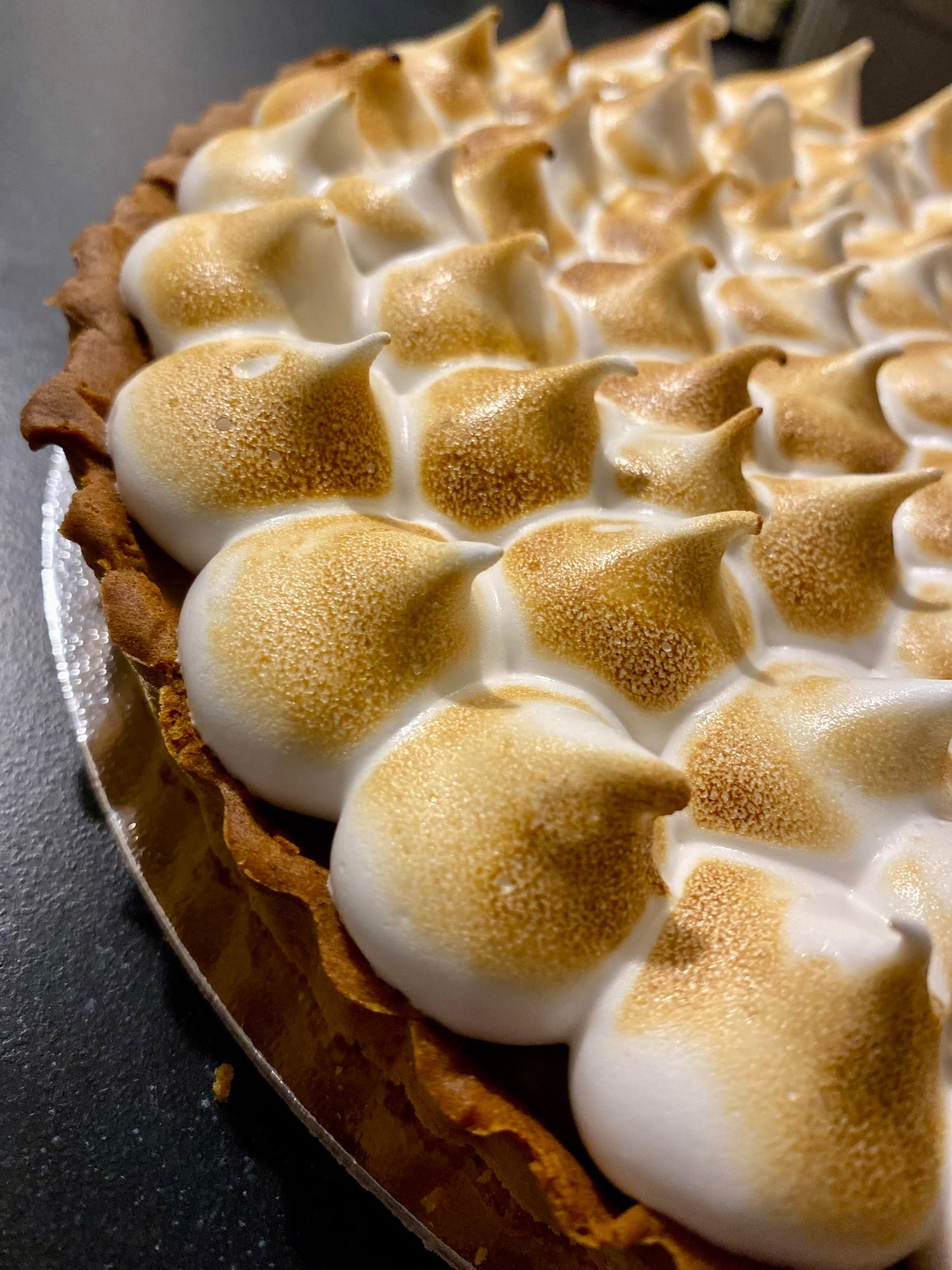A tempting slice of vegan lemon meringue pie, showcasing its bright yellow lemon curd filling and a perfectly browned, fluffy meringue topping.