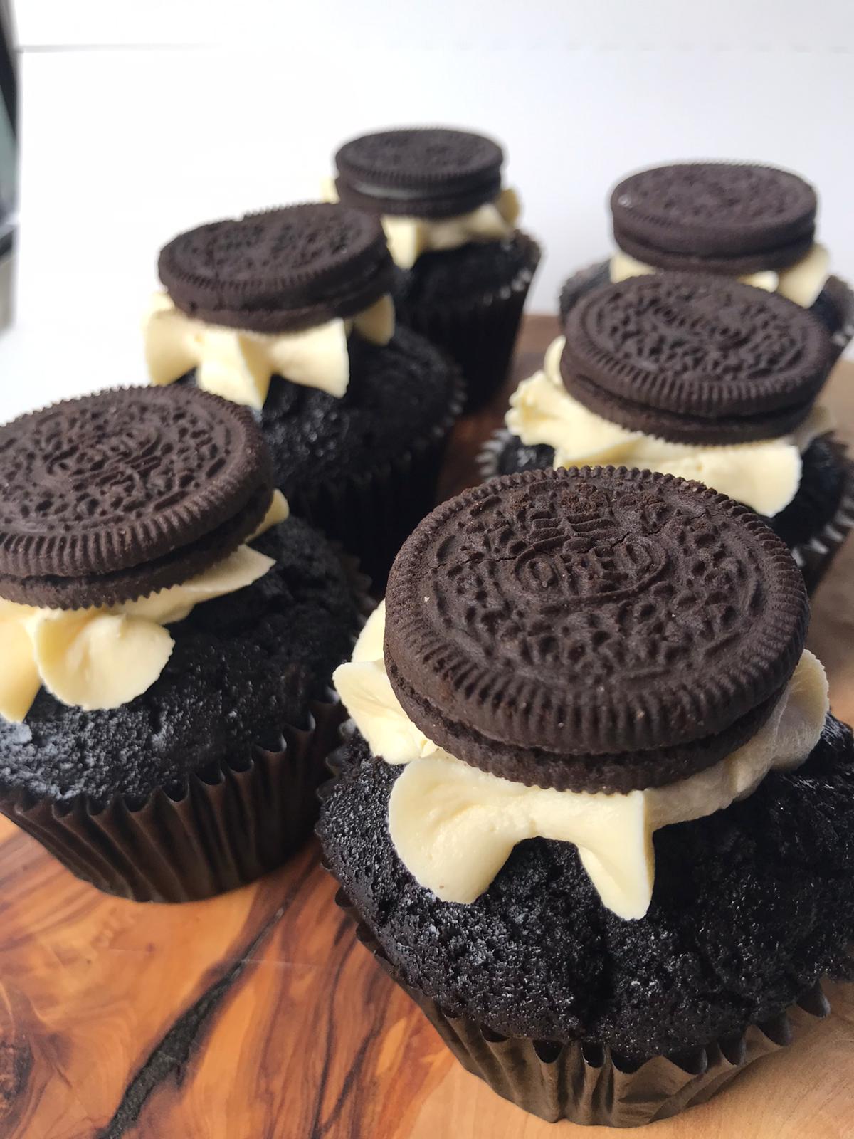 Six vegan cookies and cream cupcakes, each topped with a swirl of creamy frosting and crumbled cookies.