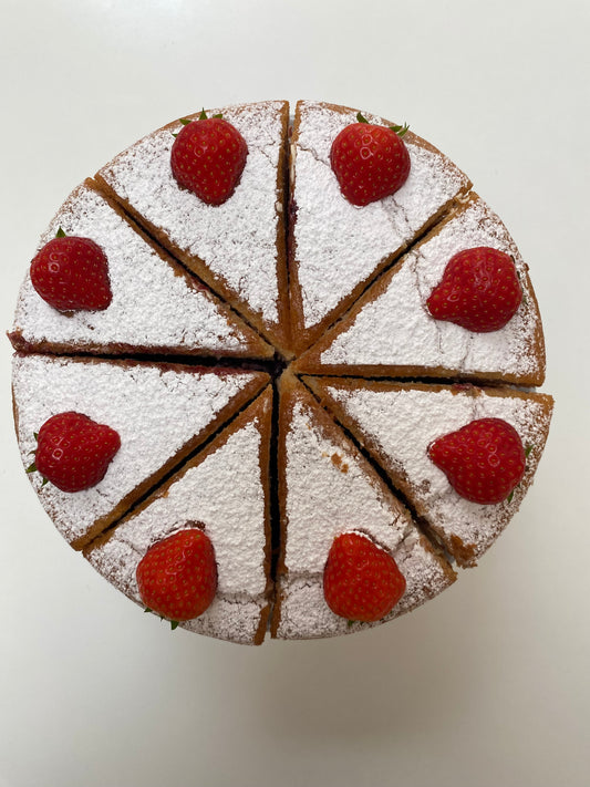 A classic Victoria Sponge Cake, cut in half to reveal a layer of raspberry jam and whipped cream between two fluffy sponge layers, dusted with powdered sugar.