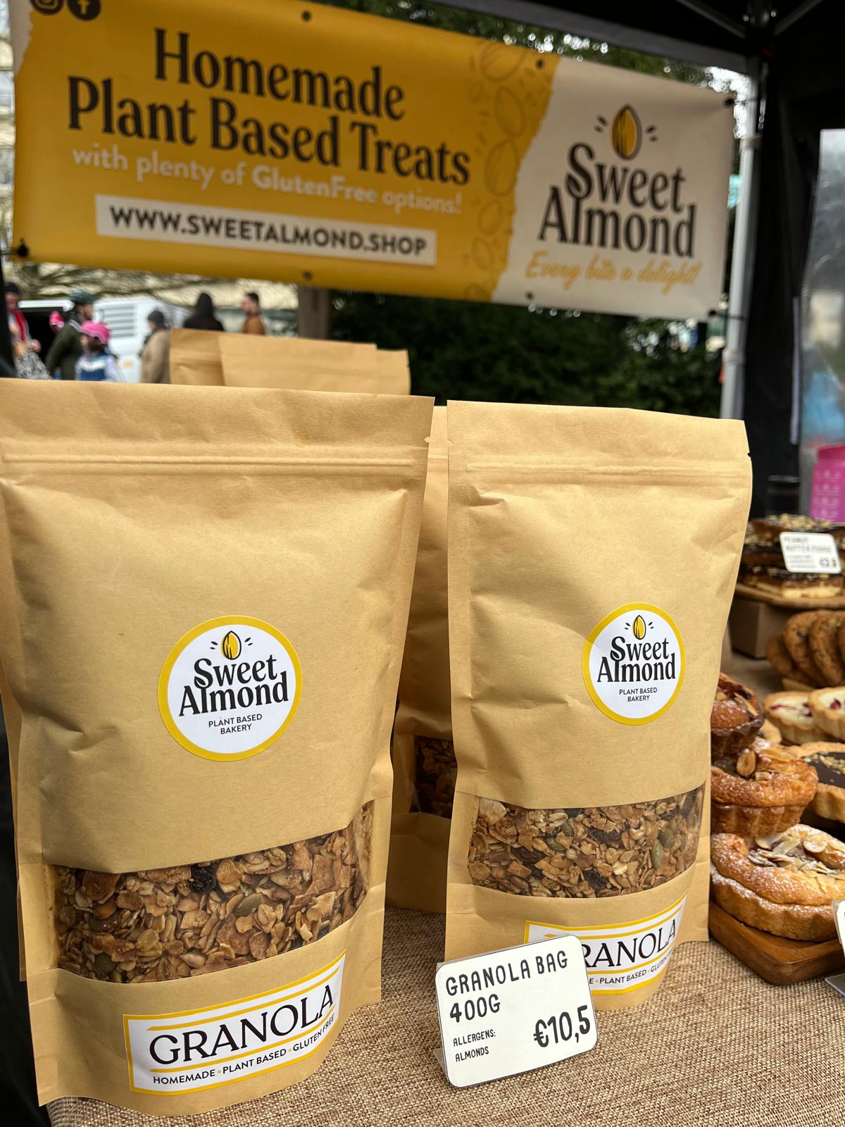 Two packages of Sweet Almond vegan granola on display with a market background.
